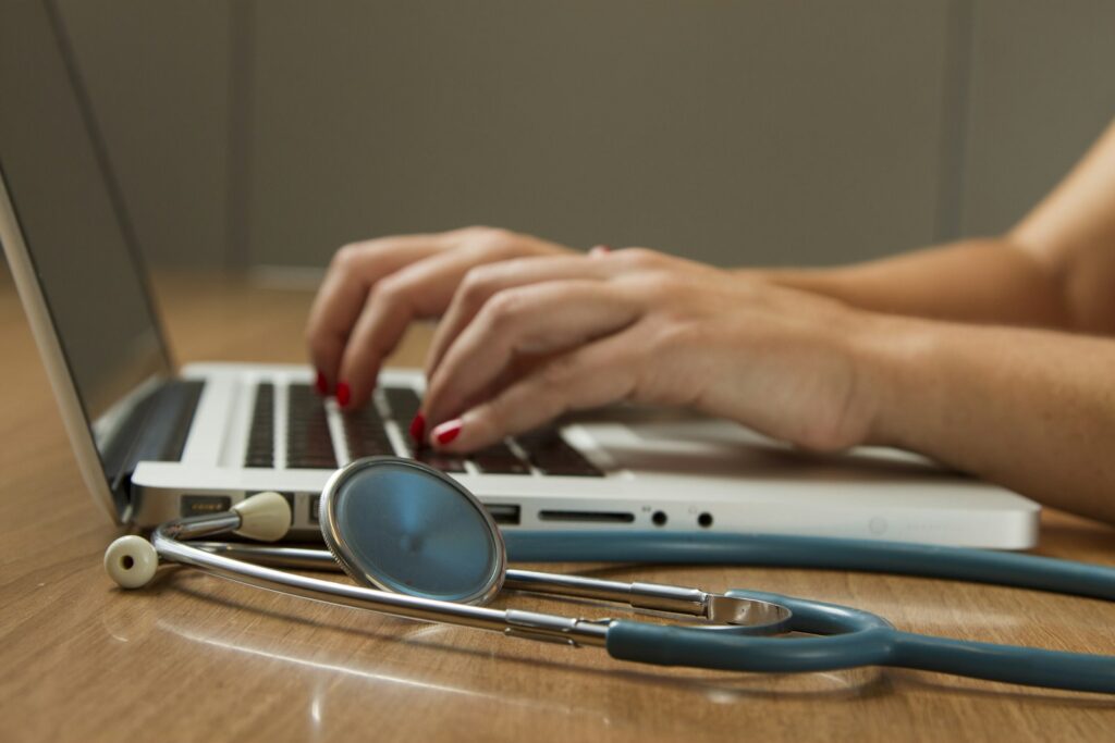 Healthcare worker using a laptop next to a stethoscope